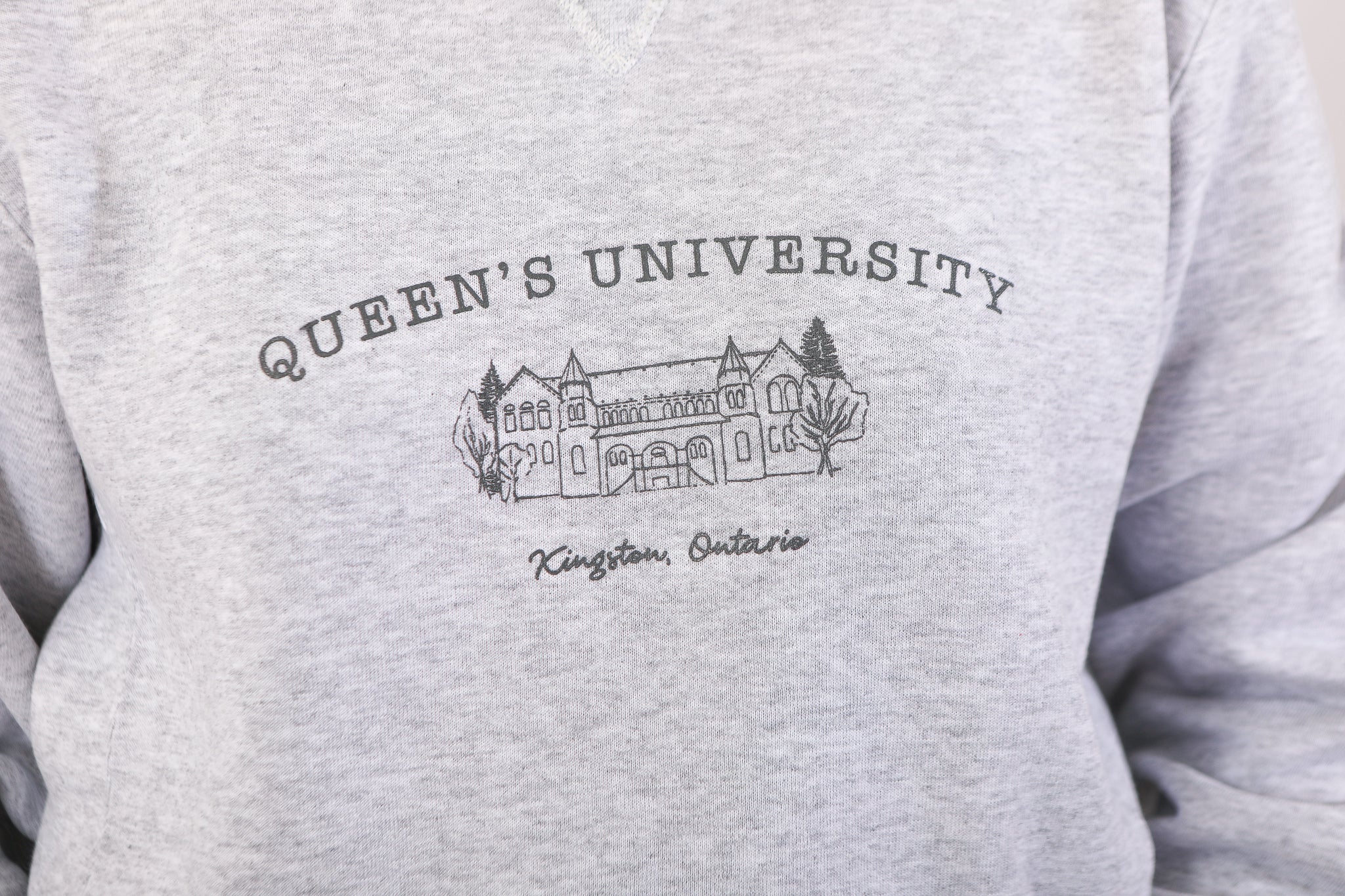 close up of model wearing a grey crewneck sweatshirt with an illustration of ontario hall